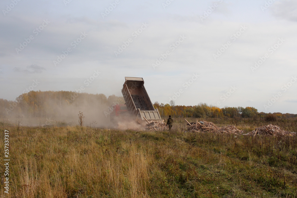 Fototapeta premium the truck dumps debris from the body of construction debris in the field violates the law harms the environment people watching