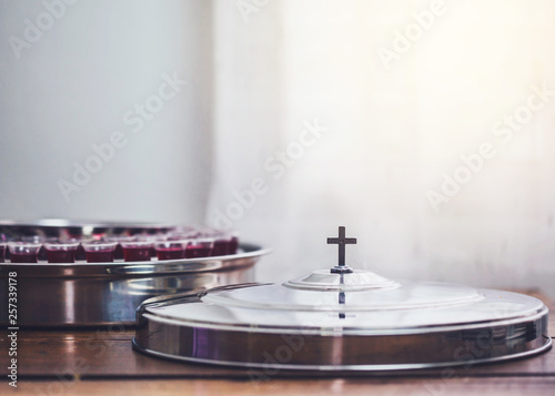 selective focus of the cross on communion tray cover with a wine glasses  in communion tray on wooden table with window light, christian background with copy space