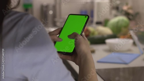 Female typing and looking for recipes internet for fresh salad on smartphone with chroma key green screen before making healthy salad, camera on slider