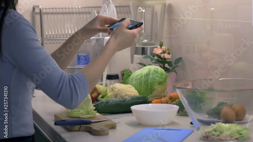 Female taking photos of healthy salad preparation on smartphone at the kitchen, cooking application. Camera on slider