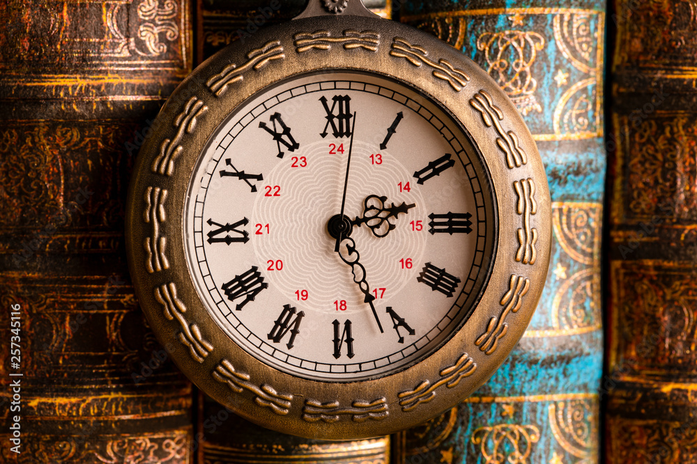 Obraz premium Antique clock on the background of vintage books. Mechanical clockwork on a chain.