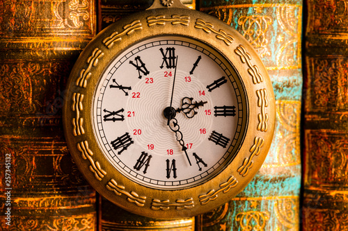 Antique clock on the background of vintage books. Mechanical clockwork on a chain.