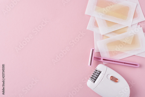 Epilator, razor and wax strips on pink background