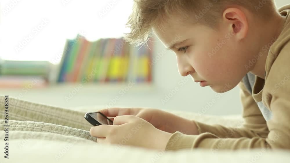 Boy looking at a smart phone while lying on the bed. Boy use a mobile phone. Internet gaming disorder. Boy looking at a smart phone while lying on the bed. Boy use a mobile phone. Internet gaming disorder.