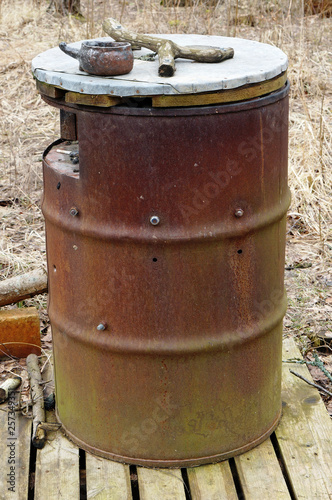 Large rusty barrel is used in the forest as a public ashtray.