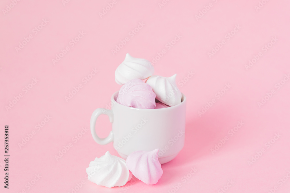 White and pink twisted meringues in a small porcelain coffe cup on pink background. French dessert prepared from whipped with sugar and baked egg whites. Greeting card with copy space White and pink twisted meringues in a small porcelain coffe cup on pink background. French dessert prepared from whipped with sugar and baked egg whites. Greeting card with copy space