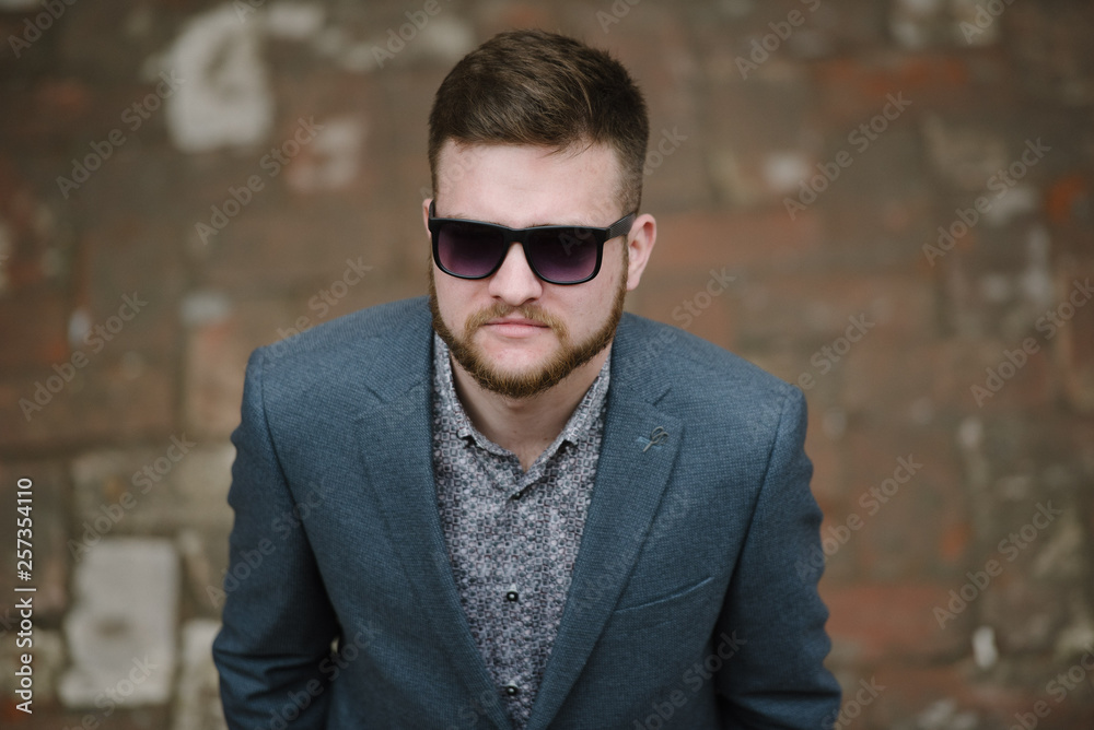 A man with a beard and sunglasses in a gray suit poses on the street to advertise men's clothing. Advertising menswear A man with a beard and sunglasses in a gray suit poses on the street to advertise men's clothing. Advertising menswear