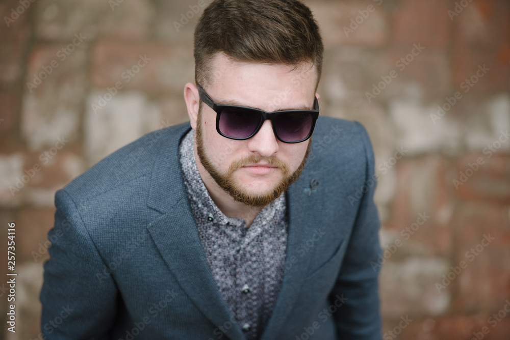 A man with a beard and sunglasses in a gray suit poses on the street to advertise men's clothing. Advertising menswear A man with a beard and sunglasses in a gray suit poses on the street to advertise men's clothing. Advertising menswear