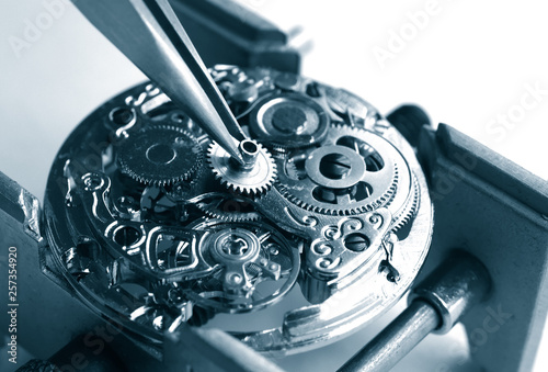 close up of watchmaker repairing old mechanical watch caliber taking small gear with tweezers photo