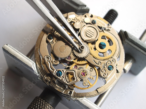 close up of watchmaker repairing old mechanical watch caliber taking small gear with tweezers photo