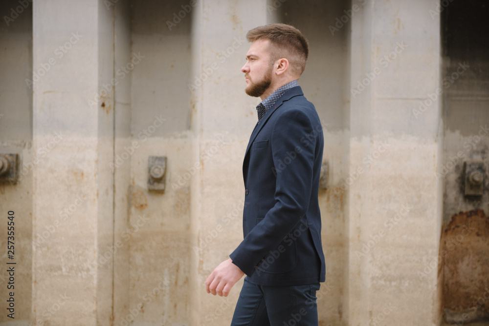 A man with a beard in a blue suit poses on the street to advertise men's clothing. Advertising menswear