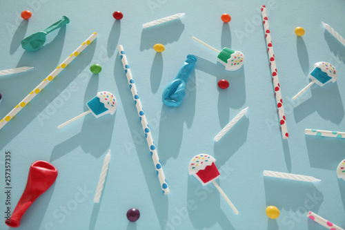 Kids birthday party decoration, blue background (pattern). Colorful candies, bright balloon, festive candles, and paper straws.