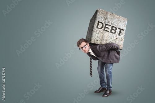 Businessman bending under a heavy stone with the word DEBT on it