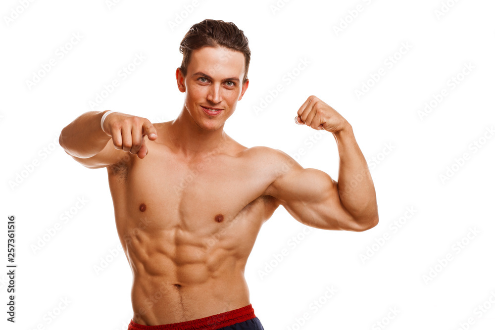 Handsome young ripped bodybuilder flexing his muscles smiling cheerfully pointing to the camera. Sexy athletic healthy man showing his biceps isolated, copy space. Gym, lifestyle, motivation concept