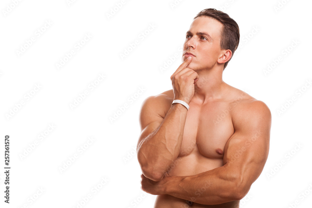 Fototapeta premium Young attractive bodybuilder posing shirtless isolated, copy space. Handsome athletic man looking away thoughtfully rubbing his chin. Sportsman thinking. Muscular man making decision. Health concept