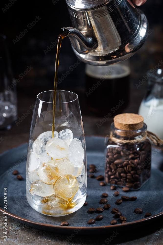 Ice coffee cold summer drink in a tall glass with pouring coffee and coffee beans on a stone background. Ice coffee cold summer drink in a tall glass with pouring coffee and coffee beans on a stone background.