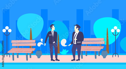two security guards smoking cigarette unhealthy lifestyle concept men colleagues in uniform standing together night urban park cityscape background full length horizontal