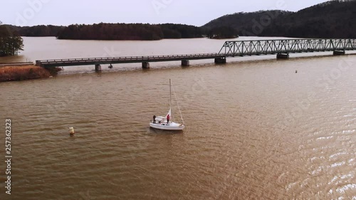 Orbital drone shot of person in red jacket raising sailboat sails on lake. photo