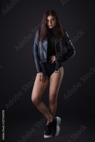 Brunette girl in a black leather jacket . Beautiful model on a dark background. Full-length studio photosession
