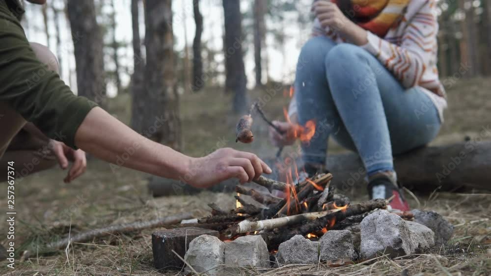 The guy with the girl preparing sausages on fire in the forest The guy with the girl preparing sausages on fire in the forest