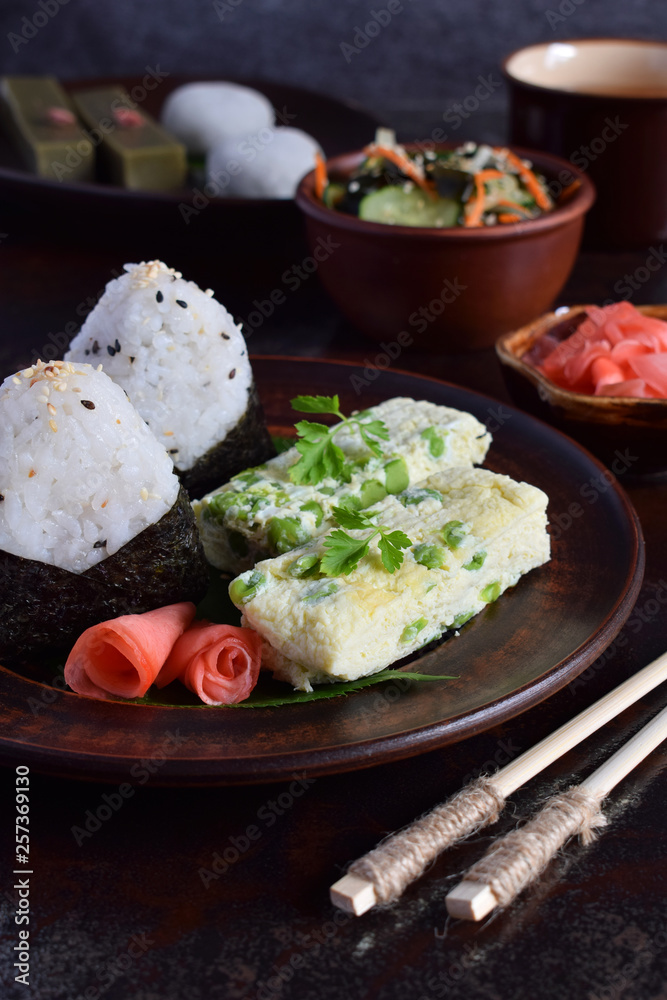 Mix of Japanese food - rice balls onigiri, omelette, ginger, sunomono wakame cucumber salad. Traditional dessert of bean and green tea matcha - jelly yokan, daifuku mochi. Asian breakfast or lunch