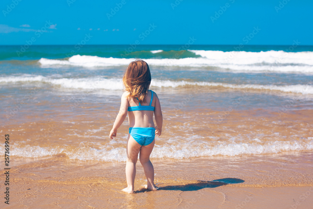 Little girl standing on the beach looking to ocean