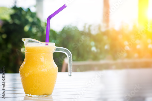 Fresh orange juice in glass in the shape of a jug with a purple straw. Smoothie on the white wooden table. photo