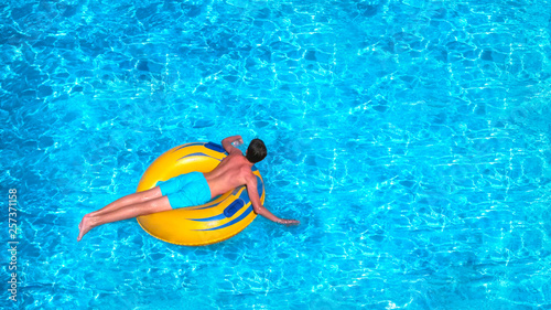 Young man is floating on yellow inflatable air ring circle in pool with blue water. Holiday leisure in happy sunny day. Vacation concept  top view.