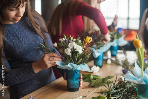 Women on the master-class on floristics. Young ladies making floral composition. Group of females with flowers indoor at the loft background. Decoration process.