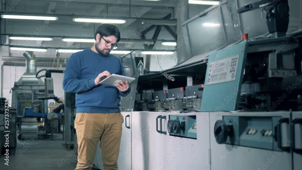 Male specialist is observing working process of a paper processing machine Male specialist is observing working process of a paper processing machine