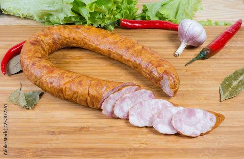 Partly sliced bologna sausage among some spices and vegetables