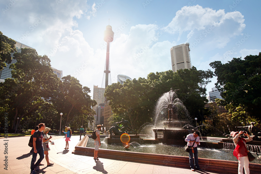 Obraz premium SYDNEY, AUSTRALIA November 20, 2017: Hyde Park Daytime Archibald fountain water reflection trees, sunbeams at Sydney TV Tower. Tourists and residents walk in the park