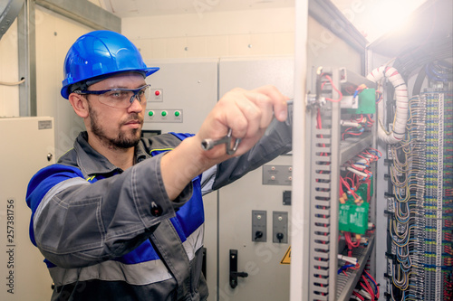 electromechanic in electrical safety gloves holds power cable, cabling connection of high voltage power electric line in industrial distribution fuseboard photo