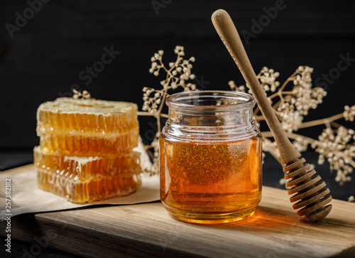 Honeycomb with honey dipper and dry flower on black background, bee products by organic natural ingredients concept