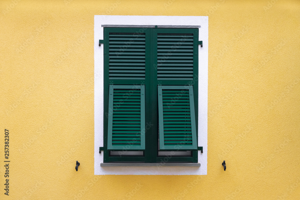 green wooden window with shutters in a white frame on the yellow wall