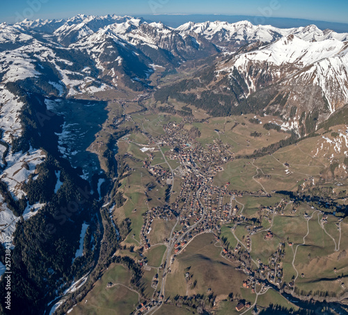 Stunning Aerial views over the a Swiss Alpine town and valley basin, surrounded by snow covered high mountain peaks and mountains.