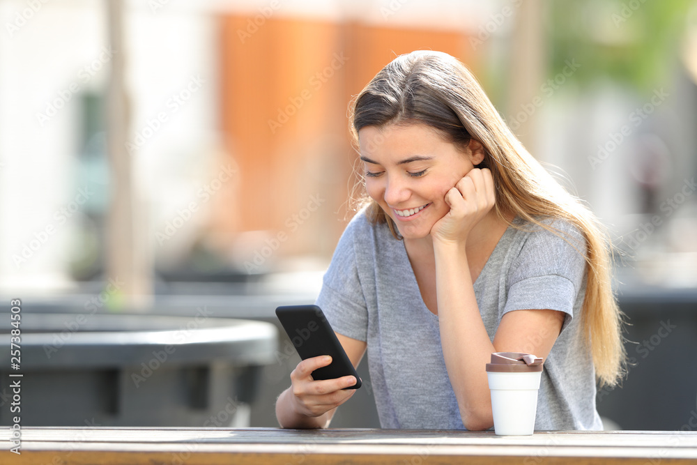 Happy teenage girl using a smart phone watching online content sitting in a park Happy teenage girl using a smart phone watching online content sitting in a park