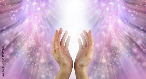 Bathing Hands in Beautiful Healing Resonance - female cupped hands reaching up into a stream of white light with shimmering sparkles flowing down on a pink ethereal energy formation background 