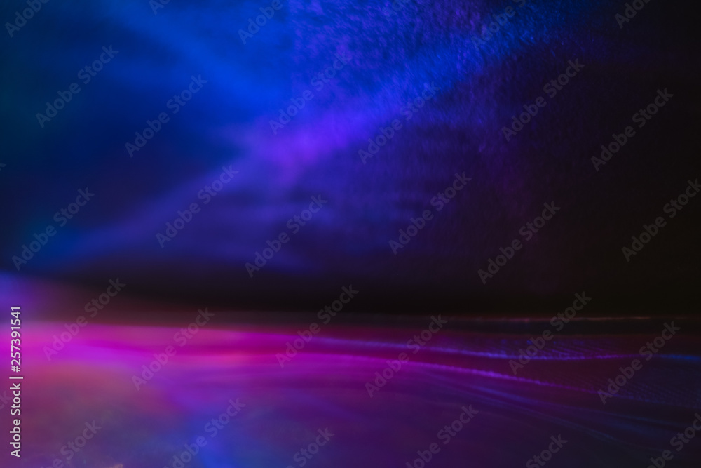 Blurred neon blue and purple abstract lines on dark background. Defocused lens flare glow effect.