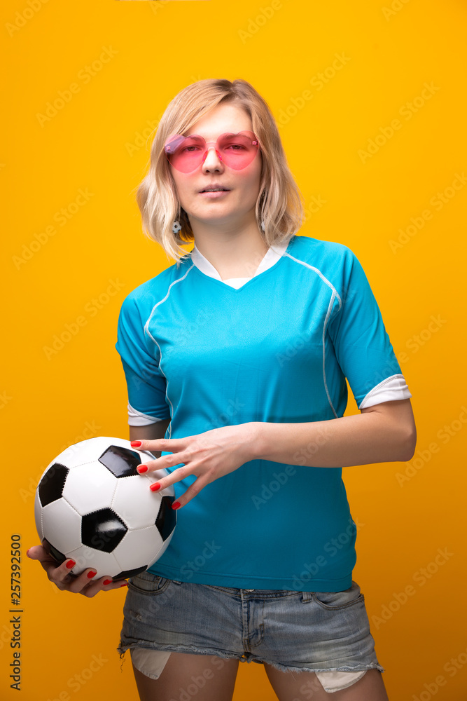 Photo of blonde in pink glasses with soccer ball on orange background Photo of blonde in pink glasses with soccer ball on orange background