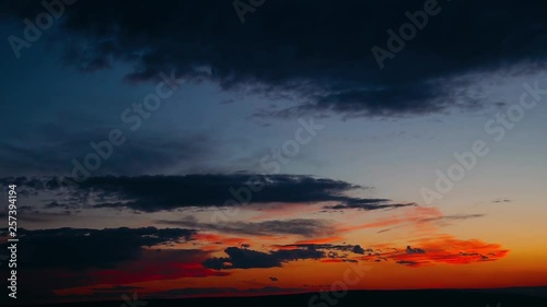 Dramatic clouds formatting storm in bright colors during sunset. Red, orange, purple sunset sky with clouds, fast motion time lapse. Cloudy Sunset over the Village and mountains photo
