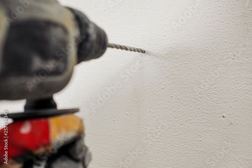 A young builder in a yellow helmet with a perforator, drills the wall in the room for repair.