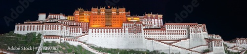 Panorama of Potala Palace at night (Lhasa, Tibet, China). Black sky, the whole palace is illuminated and shines in red and white. On top of the home of the Dalai Lama waves the Chinese flag.