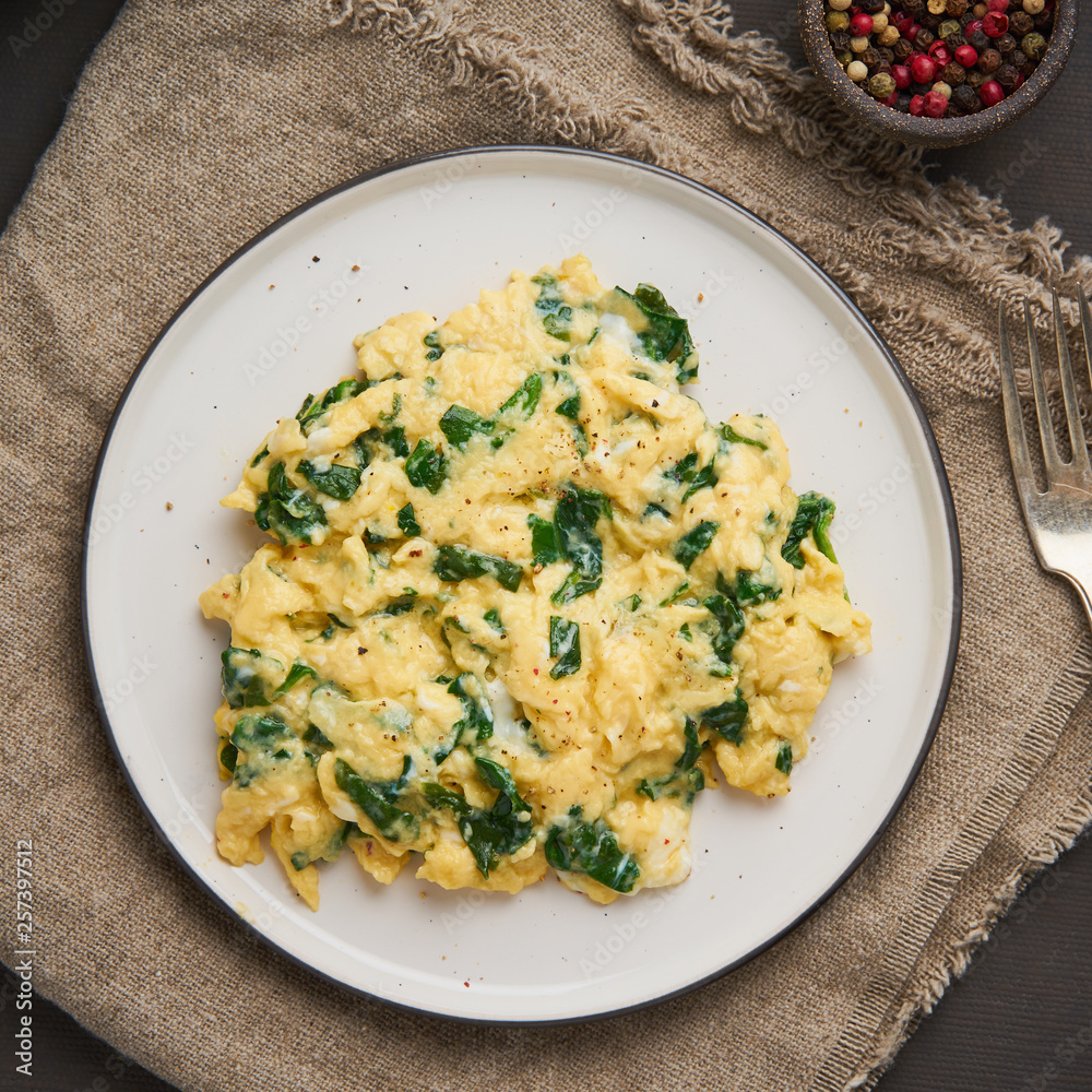 Pan-fried scrambled eggs and spinach, cup of tea on dark brown background. Breakfast with omelette, top view Pan-fried scrambled eggs and spinach, cup of tea on dark brown background. Breakfast with omelette, top view