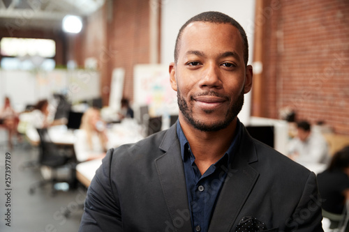 Portrait Of Businessman In Modern Open Plan Office With Business Team Working In Background