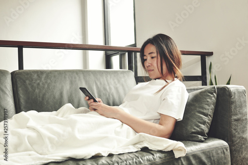 sick woman using smartphone on sofa