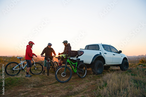 Friends Resting near Pickup Off Road Truck after Bike Riding in the Mountains at Sunset. Adventure and Travel Concept.