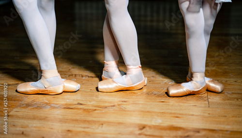 Photos Feet of a three young ballerinas in pointe shoes against the background of the wooden floor