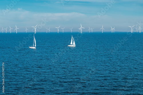 Alternative energy - row of offshore wind turbines and yachts at sea, green energy windmill generators at sea