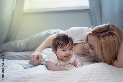 Happy smiling mother and baby lying on bed at home